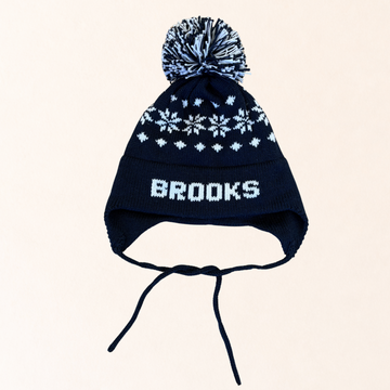 Navy blue knit hat with white snowflake pattern and 'Brooks' branding on a beige background