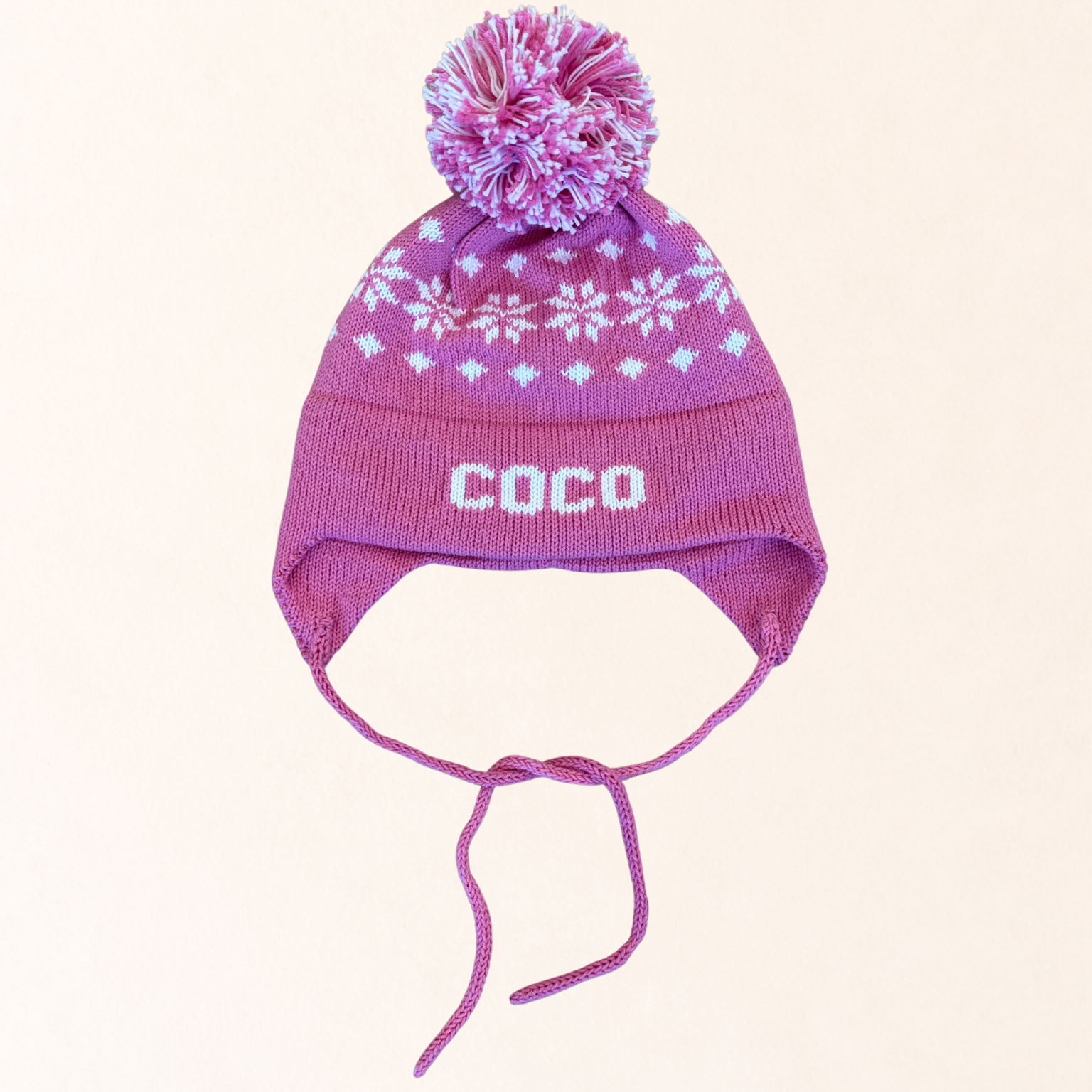 Pink knit hat with a pom-pom and 'COCO' branding on a light pink background