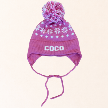 Pink knit hat with a pom-pom and 'COCO' branding on a light pink background