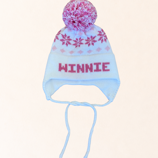 Knitted hat with floral pom-pom and 'Winnie' text on a light pink background