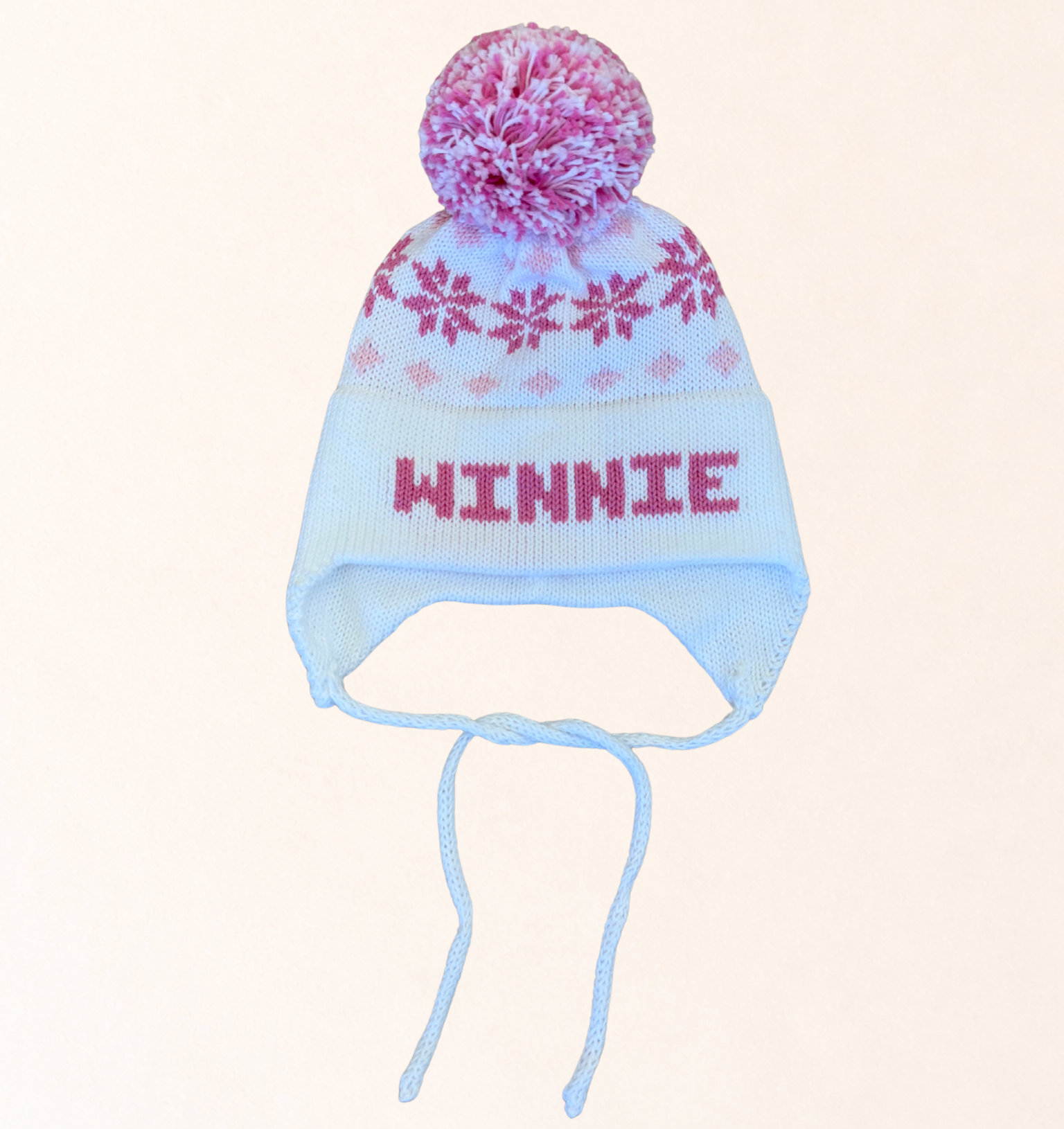 Knitted hat with floral pom-pom and 'Winnie' text on a light pink background