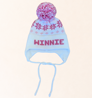 Knitted hat with floral pom-pom and 'Winnie' text on a light pink background