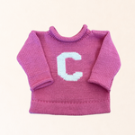 Pink knitted sweater with a white letter 'C' on a light pink background