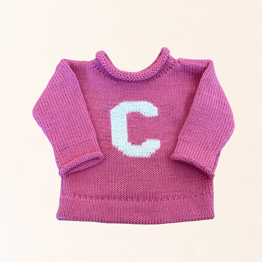Pink knitted sweater with a white letter 'C' on a light pink background