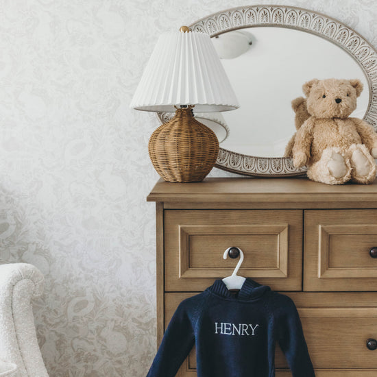 Navy knit sweater for kids personalized with the name "Henry" in white stitching hanging on a dresser drawer