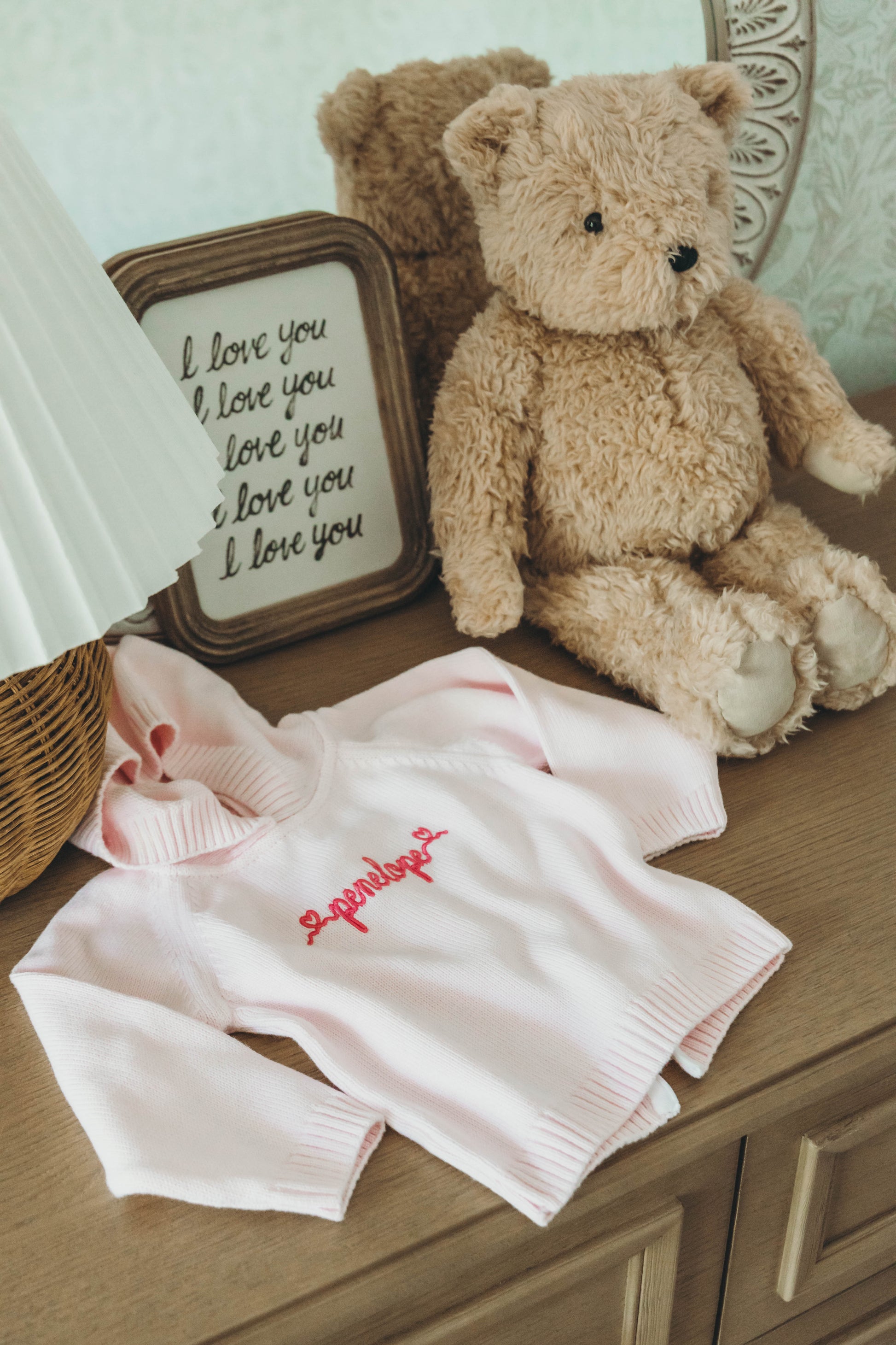 Pink knit sweater for kids personalized with the name "penelope" in dark pink cursive on a dresser