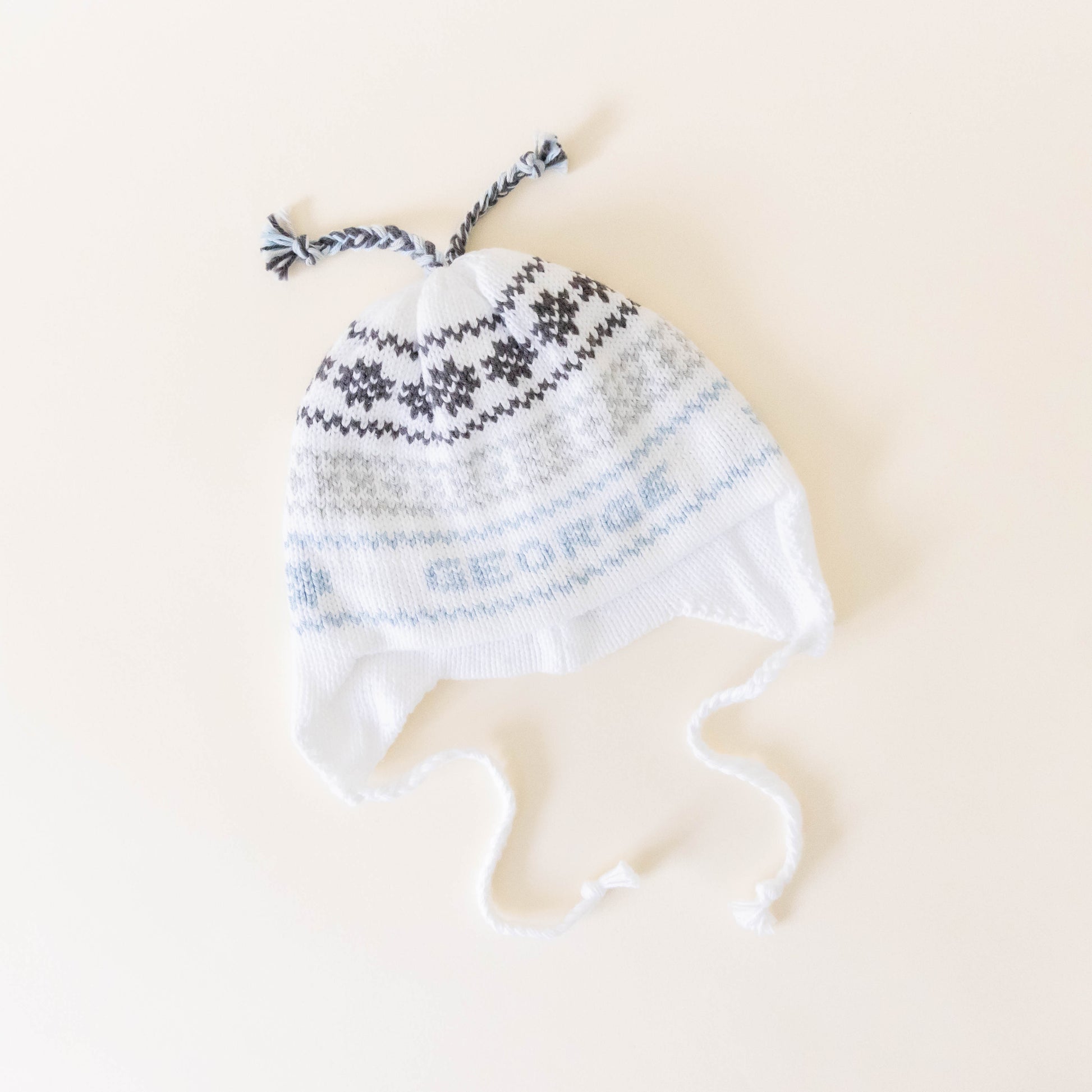 White knit hat with blue and grey stitching on a neutral background laying flat