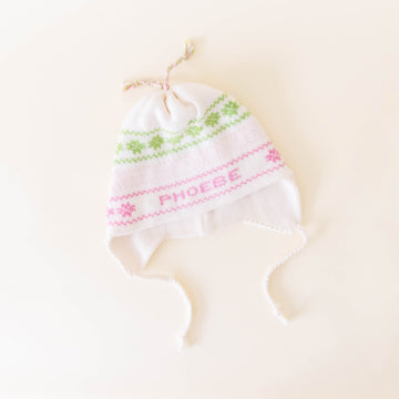 White knit hat with pink and green stitching personalized with the name "Phoebe" on a neutral background