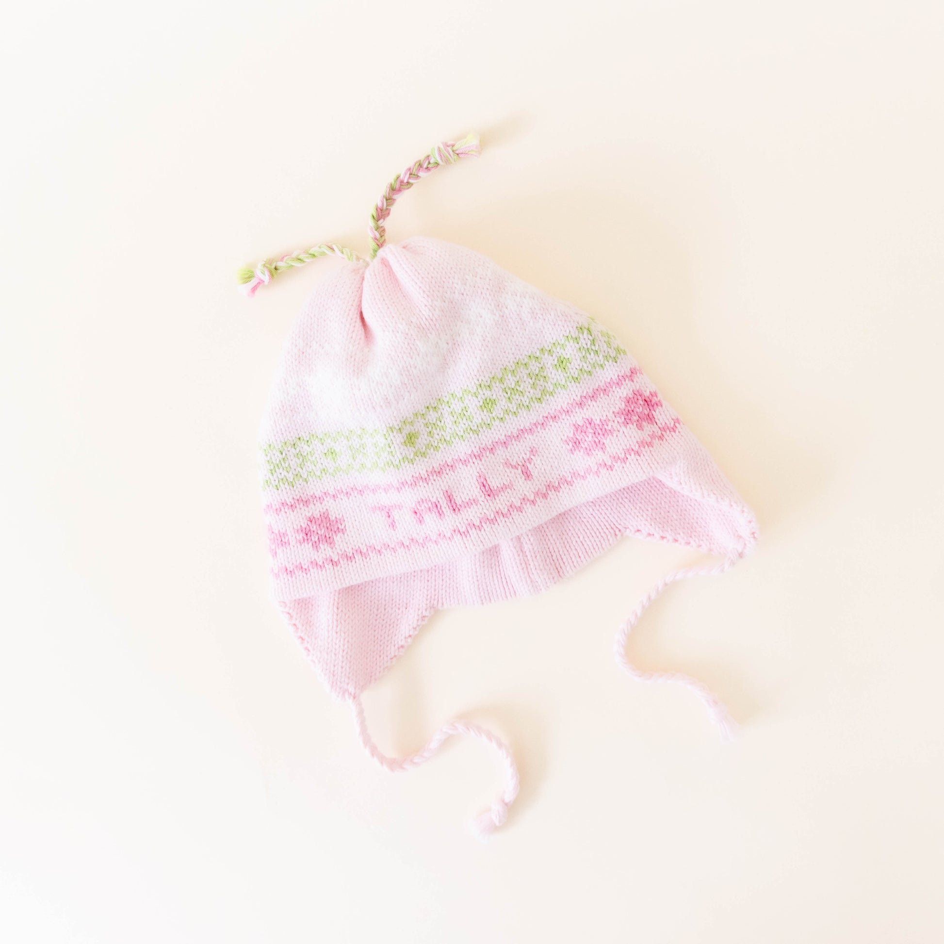 Pink knit hat with pink and green stitching personalized with the name "Tally" on a neutral background