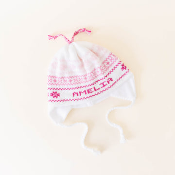 White knit hat with pink stitching personalized with the name "Amelia" on a neutral background