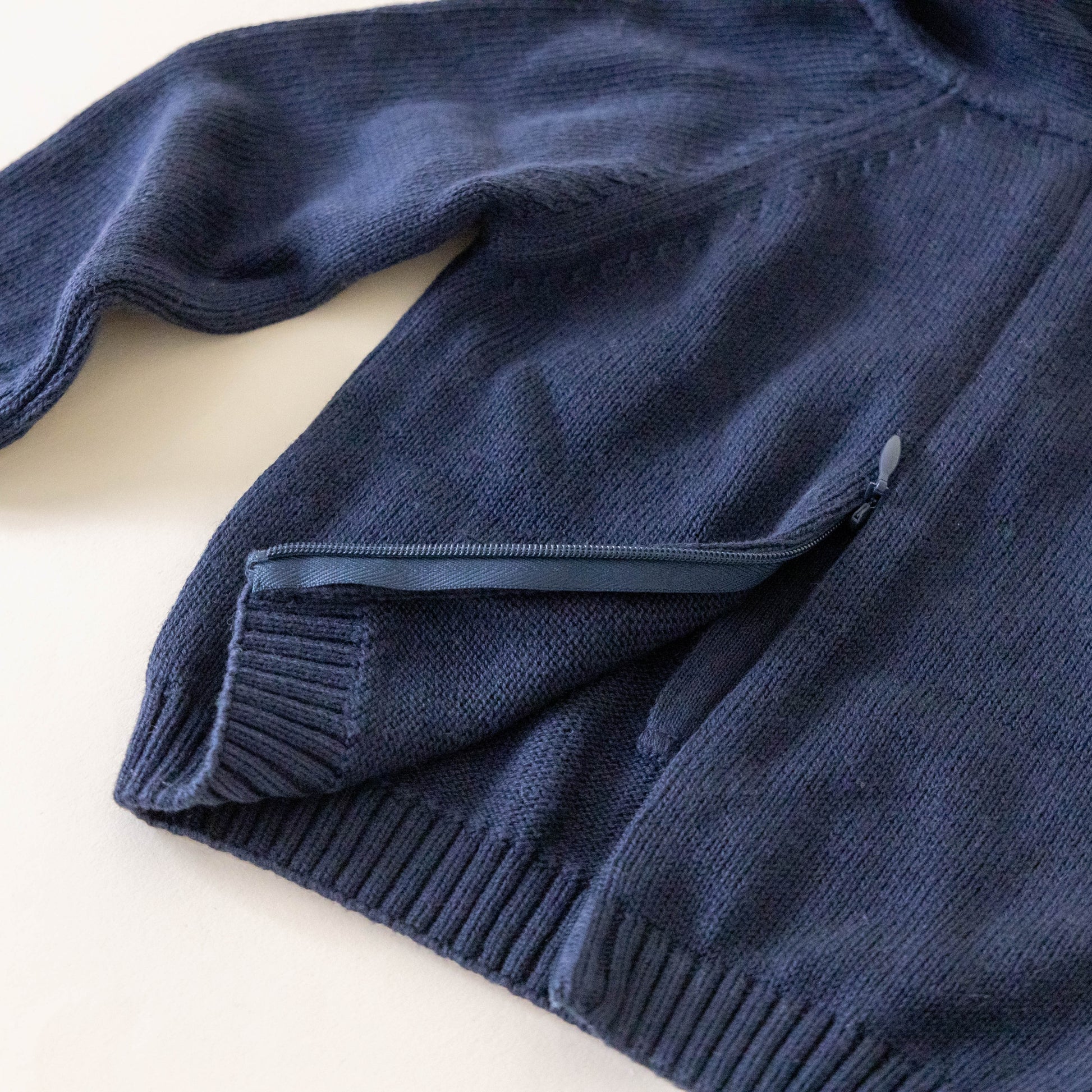 Back of navy knit sweater for kids showing a zipper on a neutral background