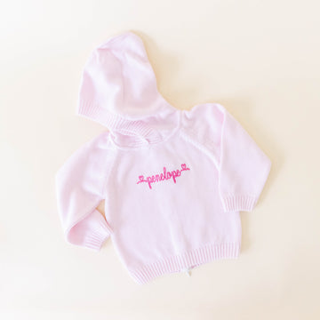 Pink knit sweater for kids personalized with the name "penelope" in dark pink cursive on a neutral background