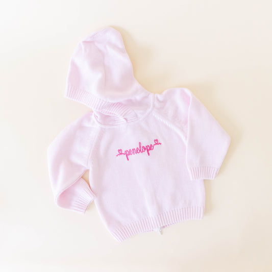 Pink knit sweater for kids personalized with the name "penelope" in dark pink cursive on a neutral background