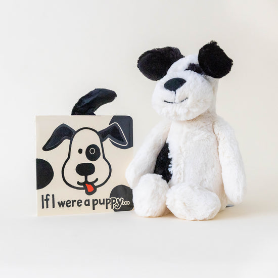 Black and cream puppy stuffed animal with a book titled "If I were a puppy" on a neutral background