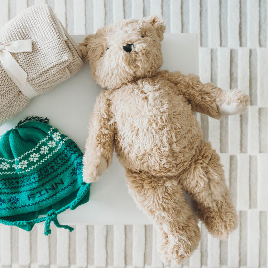 Green knit hat personalized with the name "Finn" on a nightstand with a teddy bear