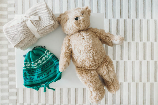 Green knit hat personalized with the name "Finn" on a nightstand with a teddy bear