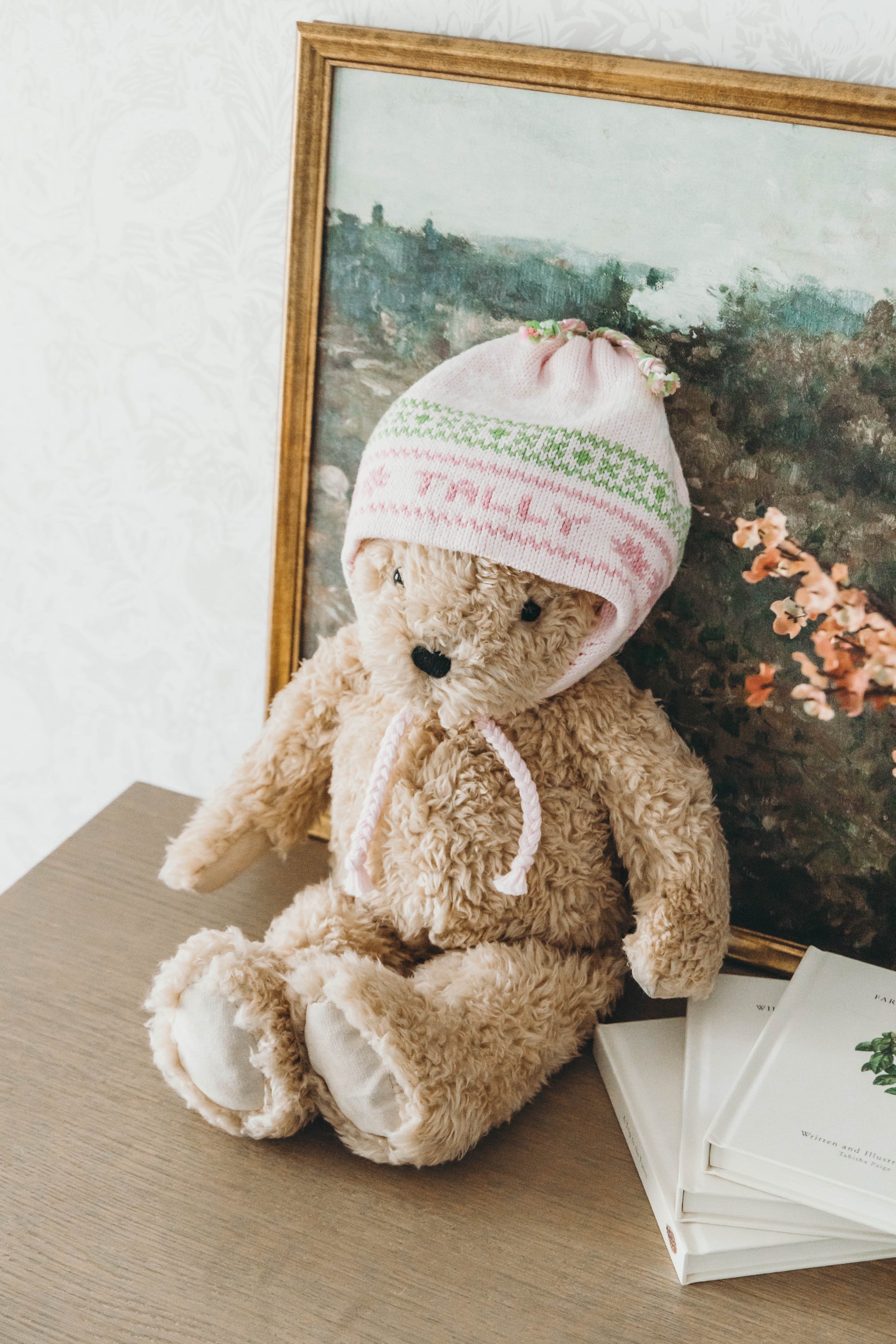 Pink knit hat with pink and green stitching personalized with the name "Tally" worn on a teddy bear