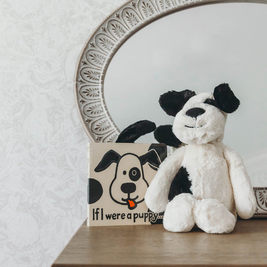 Black and cream puppy stuffed animal with a book titled "If I were a puppy" on a dresser