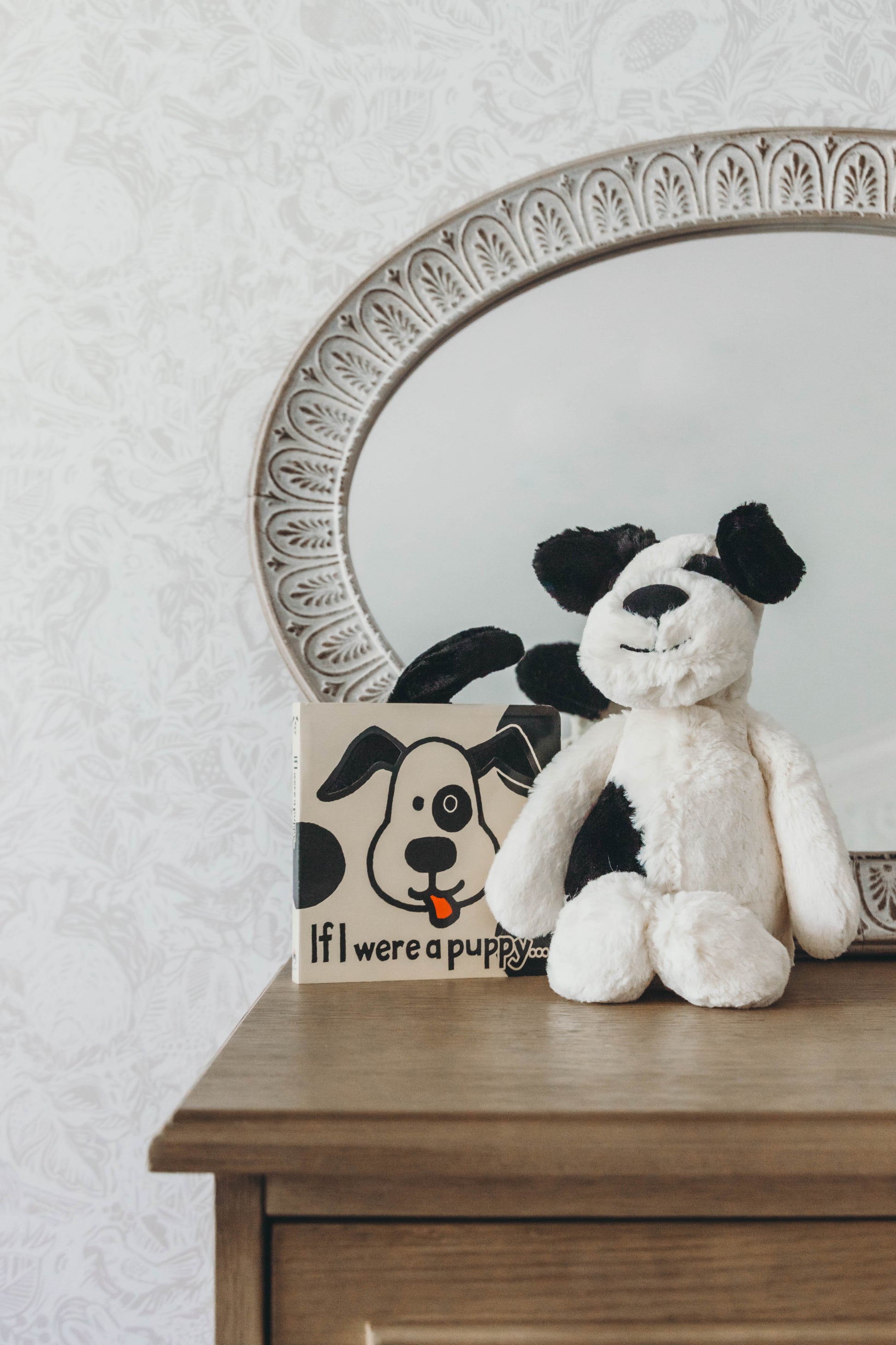 Black and cream puppy stuffed animal with a book titled "If I were a puppy" on a dresser